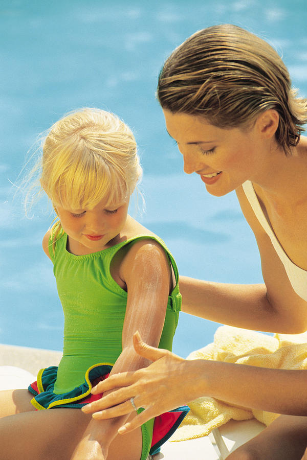 Mother applying suntan lotion to child sitting by pool Photograph by Comstock