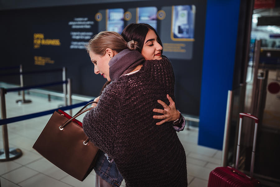 Mother embracing teenage daughter ready for departure at airport Photograph by Wundervisuals