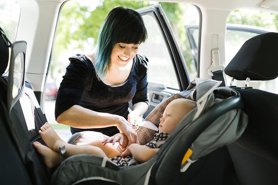 Mother fastening baby boy (12-17 months) in car seat Photograph by Jessica Peterson