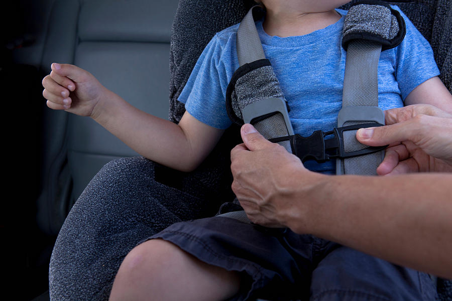 Mother fastening child safety seat belt in car Photograph by David Jakle