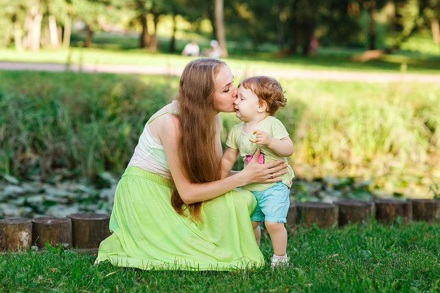 Mother kisses daughter in park on green lawn Photograph by Snedorez