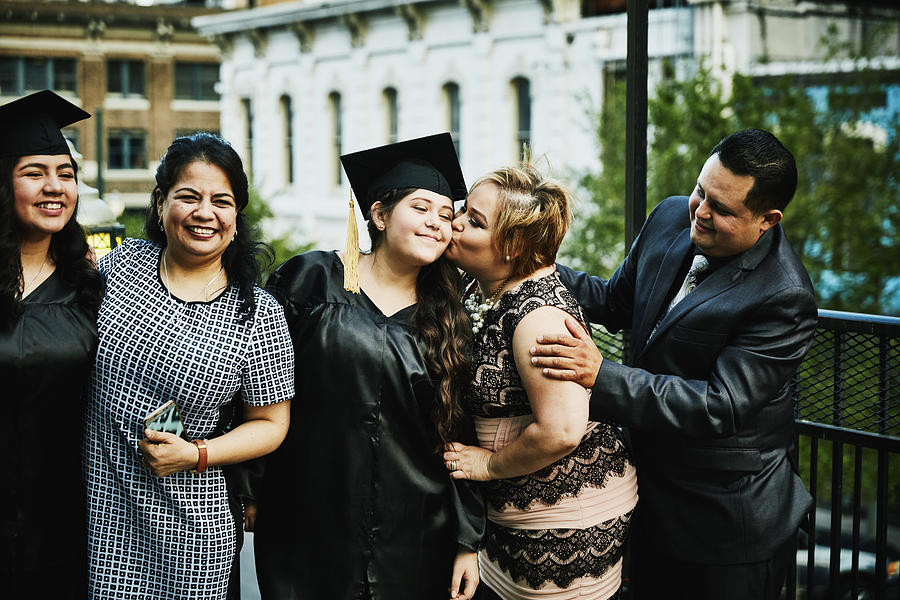 Mother kissing graduating daughter during family celebration on restaurant deck Photograph by Thomas Barwick