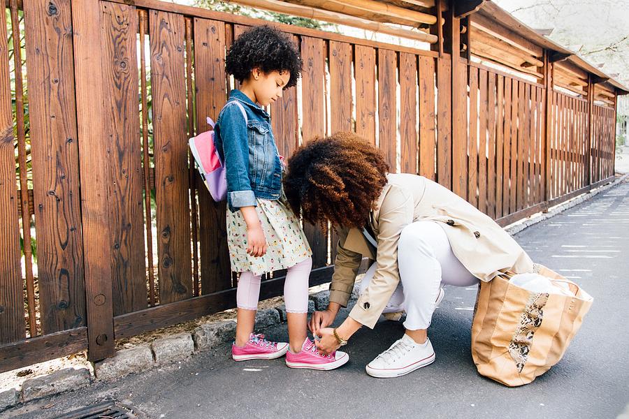 Mother kneeling by fence tying daughters shoelace Photograph by Ashley Corbin-Teich