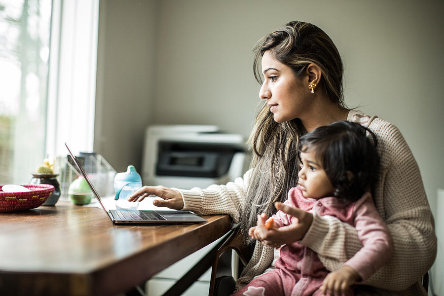Mother multi-tasking with infant daughter in home office Photograph by MoMo Productions