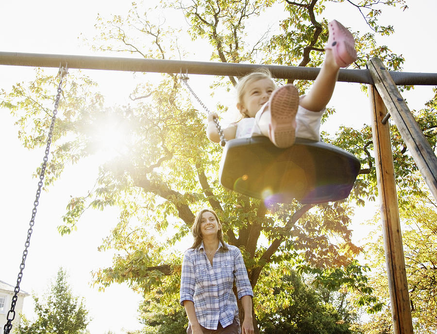 Mother pushing daughter on swing in sunny park Photograph by Anthony Lee