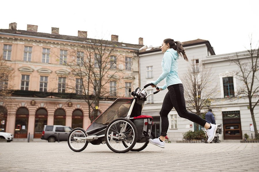 Mother running with child in stroller in the city Photograph by Westend61