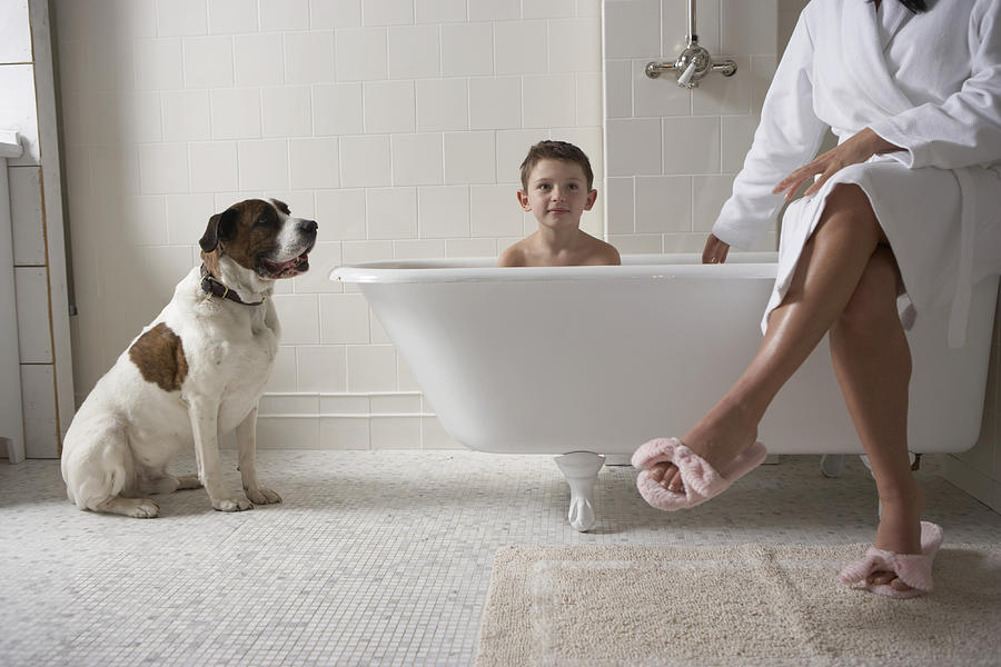 Mother sitting on side of tub with son (6-8) in bath tub and with dog Photograph by Chris Amaral