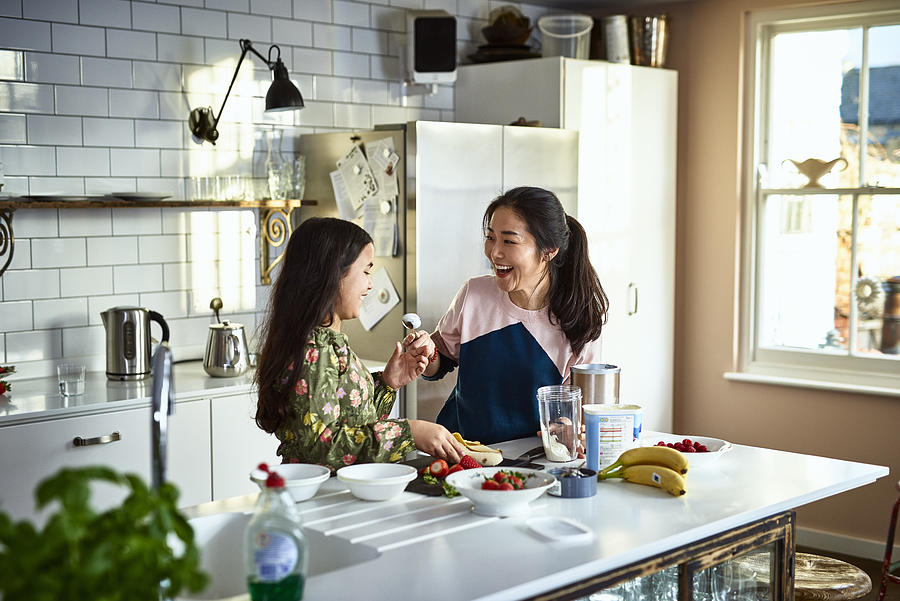 Mother teasing daughter in kitchen whilst making smoothies Photograph by 10000 Hours