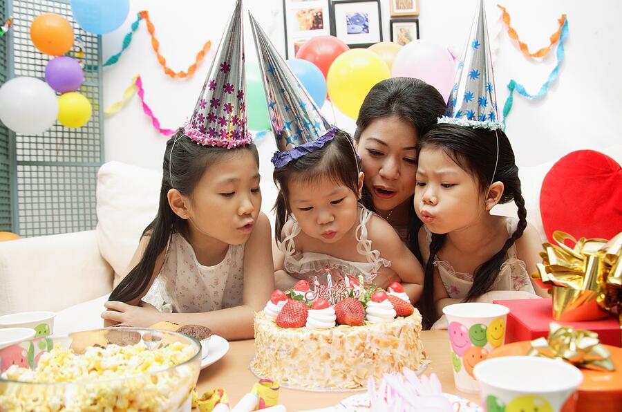 Mother with three girls celebrating a birthday, blowing candles on cake Photograph by Asia Images Group