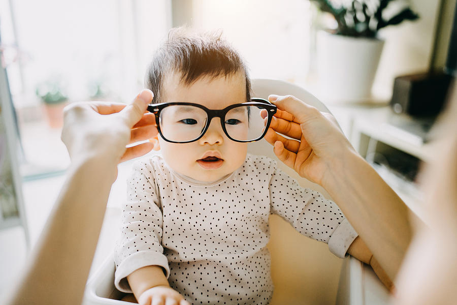 Mothers hand putting on oversized glasses onto baby girl Photograph by D3sign