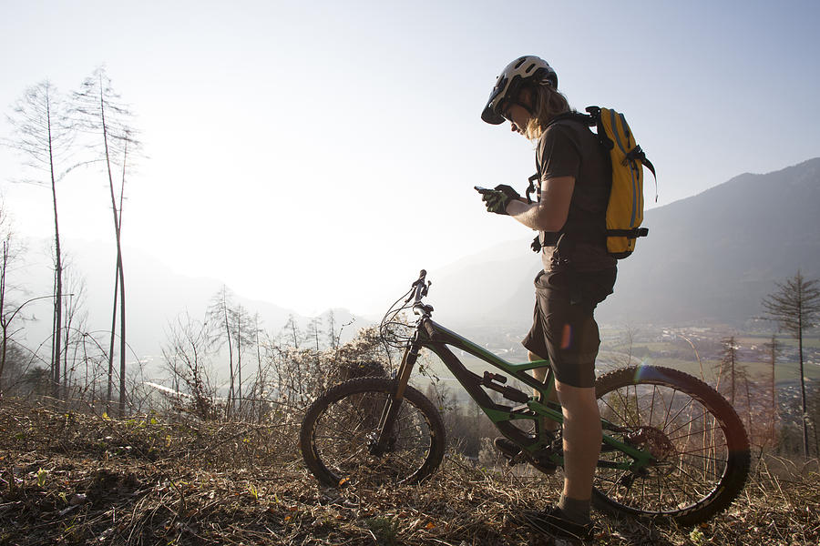 Mountain biker sends text from forest track, mountains Photograph by Ascent/PKS Media Inc.