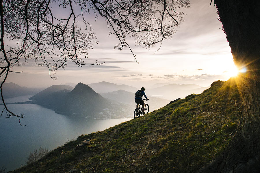 Mountain biker traverses steep mountain slope above lake Photograph by Milo Zanecchia/ Ascent Xmedia