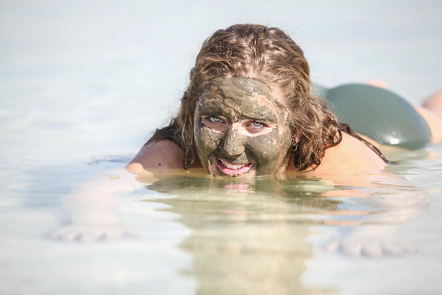 Mud covered female tourist floats in the Dead Sea, Israel Photograph by PhotoStock-Israel
