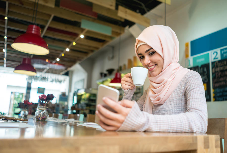 Muslim woman at a cafe texting on her mobile phone Photograph by Andresr