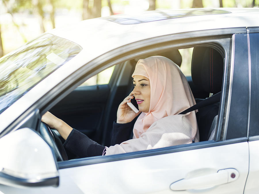 Muslim woman using smart phone while driving car Photograph by Ozgurdonmaz