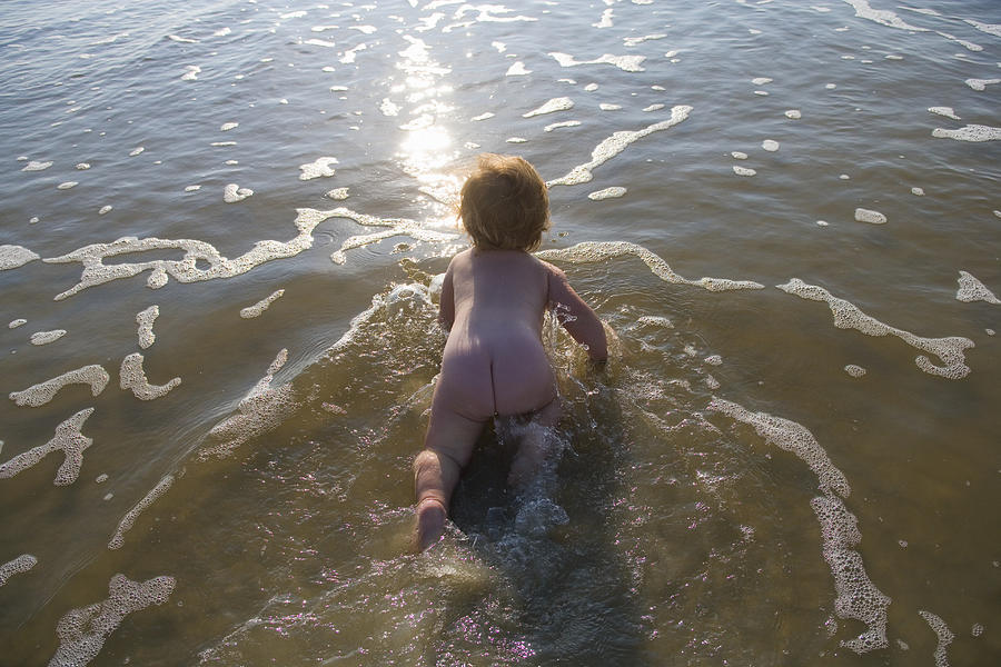 Naked baby girl (9-12 months) crawling through water Photograph by Marc Romanelli