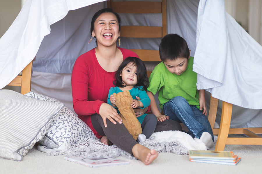 Native American mom plays with her daughter and son under makeshift fort in living room Photograph by FatCamera