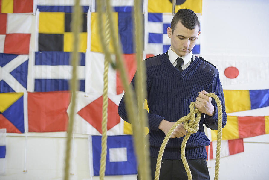 Nautical student standing in front of signalling flags and tying reef knot with rope Photograph by Monty Rakusen