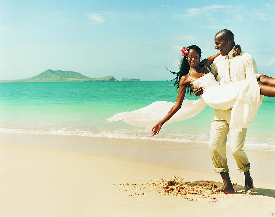 Newlywed Couple Messing About in the Sand at the Waters Edge on a Beach Photograph by Digital Vision.