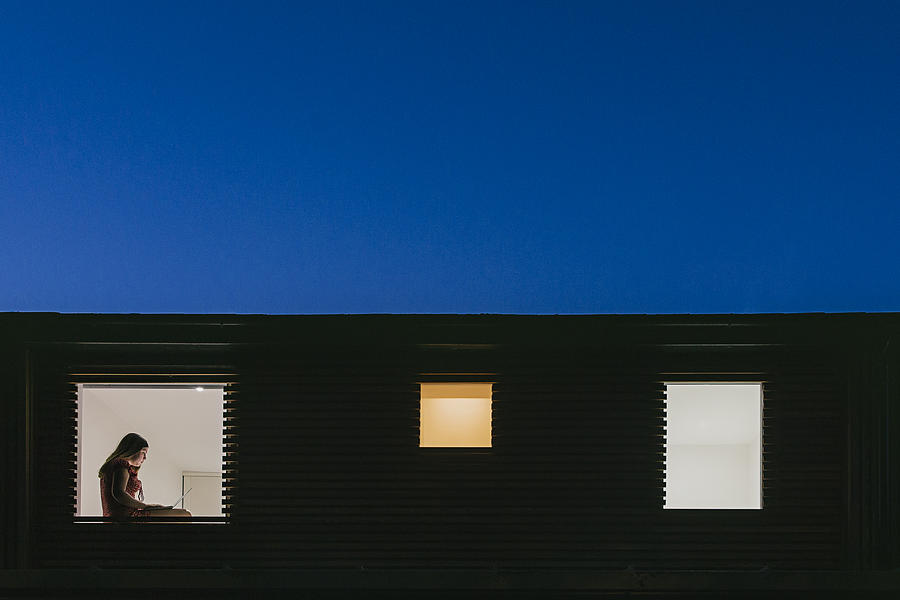 Night time view of home exterior - figure on laptop in the window Photograph by Justin Paget