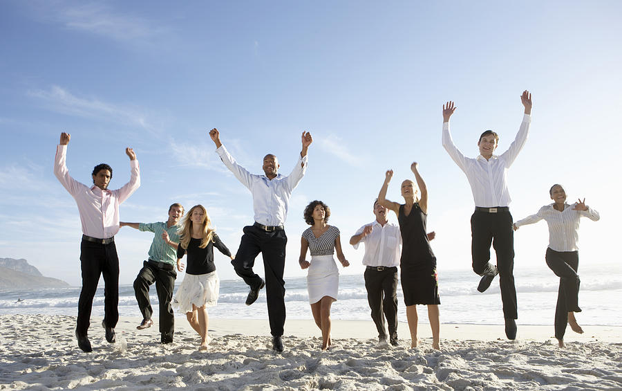 Nine businessmen and women jumping on beach, smiling Photograph by Plustwentyseven