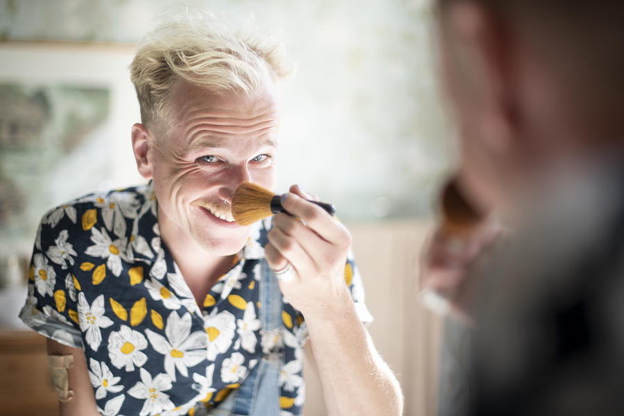 Non-binary person powdering their nose, looking into the camera via the mirror with a cheeky smile Photograph by Lucy Lambriex
