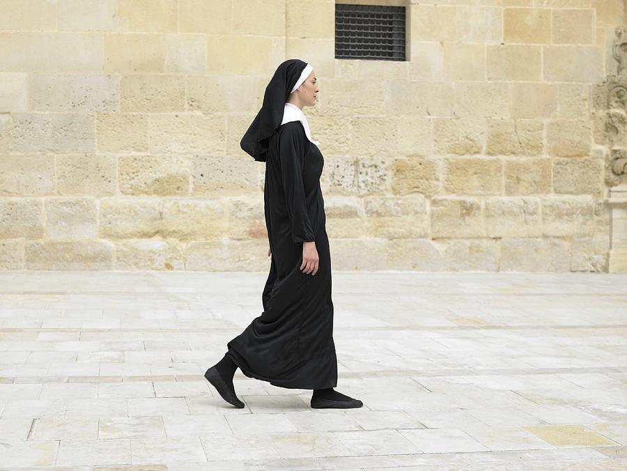 Nun walking in front of stone wall, Alicante, Spain, Photograph by Dev Carr