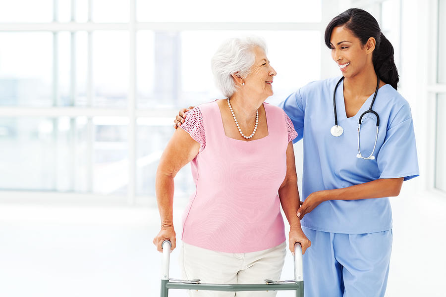 Nurse Assisting Elderly Woman With Walker While Looking At Her Photograph by Neustockimages