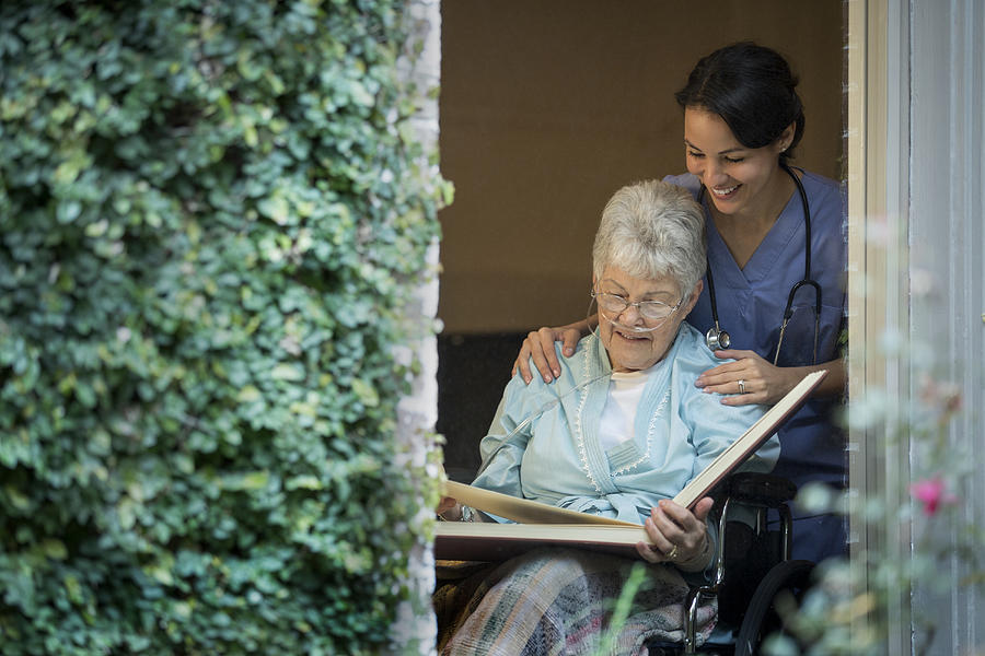 Nurse looking at photo album with woman in wheelchair Photograph by Terry Vine