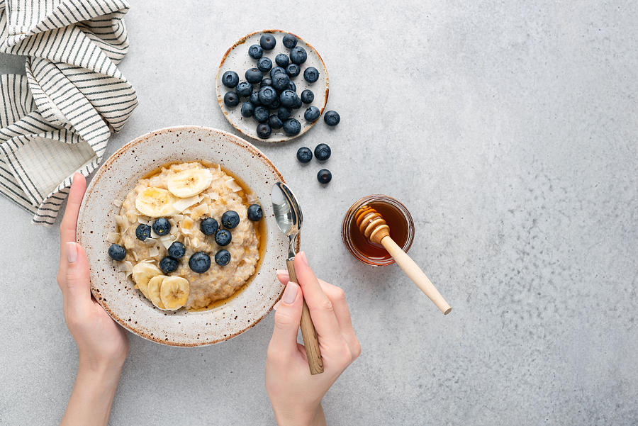 Oatmeal porridge bowl with blueberries in female hands Photograph by Arx0nt