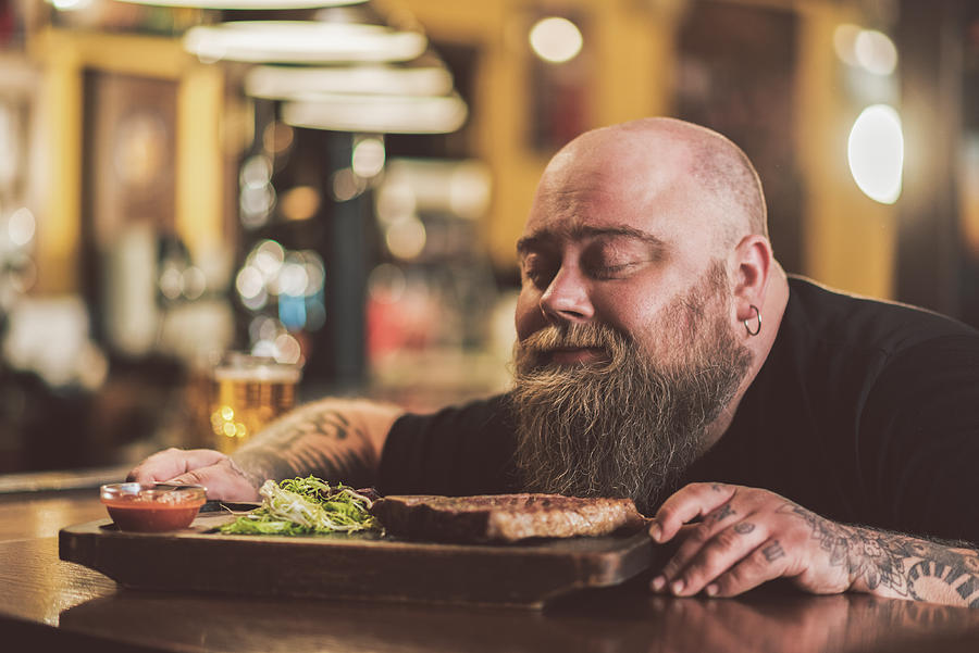 Obese male savoring grilled meat in pub Photograph by YakobchukOlena