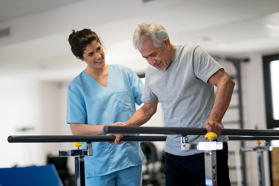 Occupational therapist and senior patient working out using parallel bars to walk Photograph by Andresr