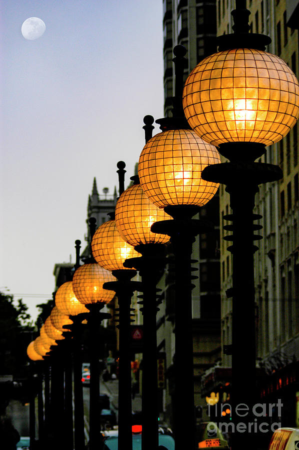 Old fashioned street lights lined up in a row as dusk turns into evening.  Photograph by Gunther Allen