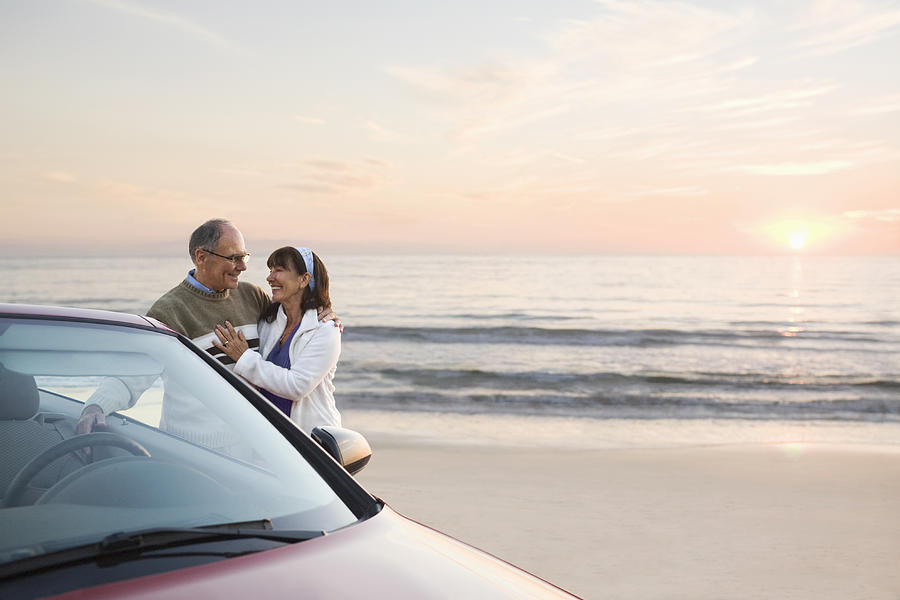 Older couple standing at car on beach Photograph by PBNJ Productions
