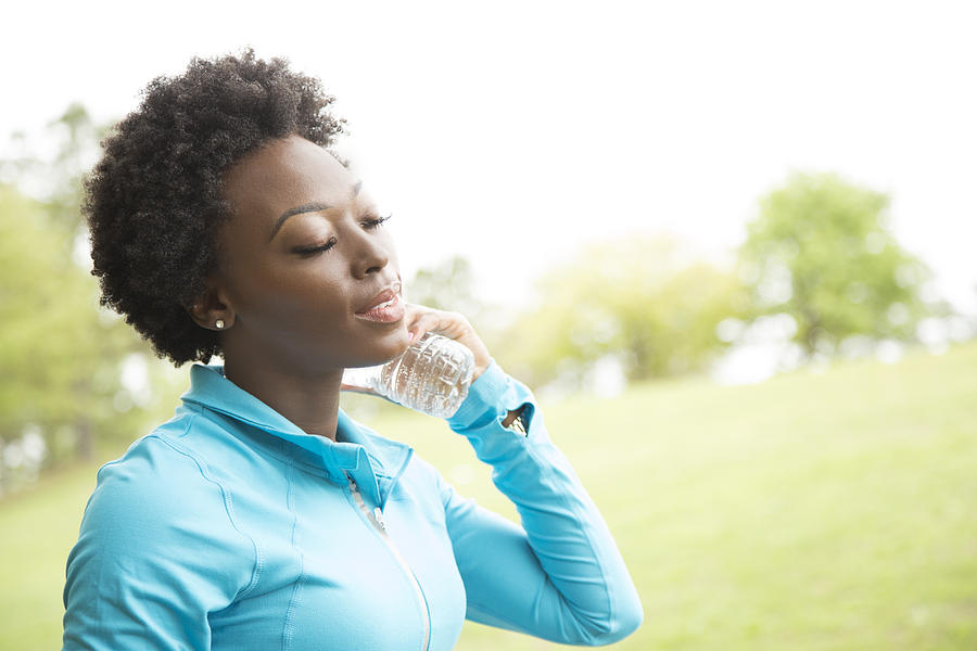 One African descent woman takes water break in neighborhood park. Photograph by Fstop123