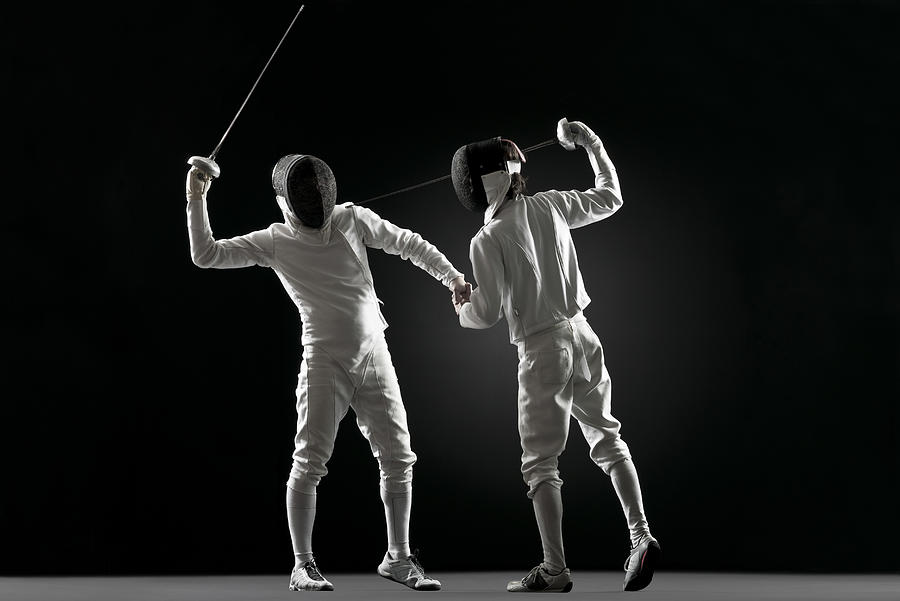 One fencer pointing fencing foil at the other fencer Photograph by PhotoAlto/Milena Boniek