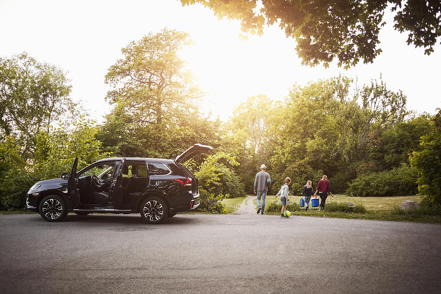 Open black electric car with family walking in park Photograph by Maskot