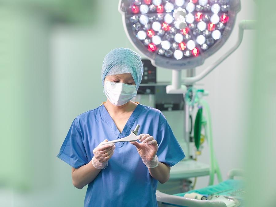 Orthopaedic nurse in operating theatre with replacement hip stem Photograph by Monty Rakusen