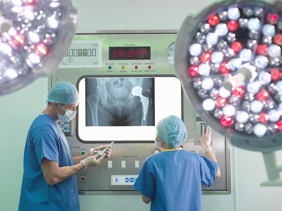 Orthopaedic surgeon and nurse with replacement hip stem in operating theatre Photograph by Monty Rakusen