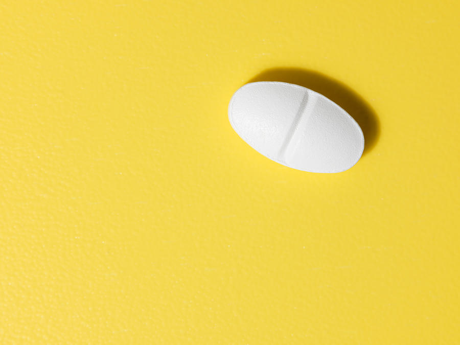 Oval white pill on yellow background Photograph by Navinpeep
