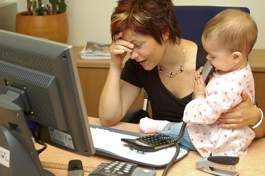 Overcharged, working mother with child in office Photograph by Michaela Begsteiger