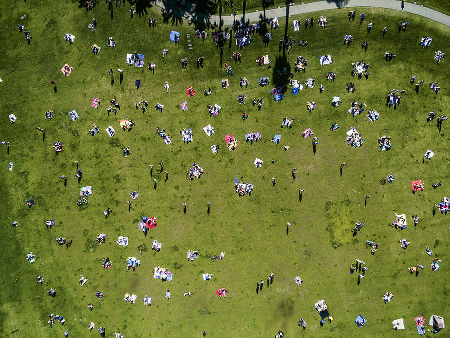 Overhead view of people in a city park on a summer day, sitting, standing, on picnic rugs. Photograph by Mint Images