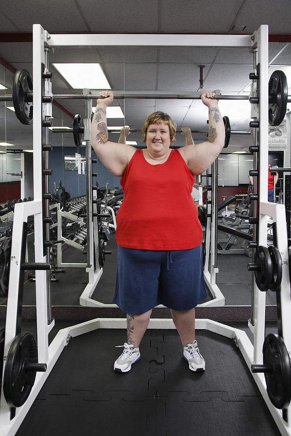 Overweight woman exercising with barbell in gym, portrait Photograph by Gravity Images