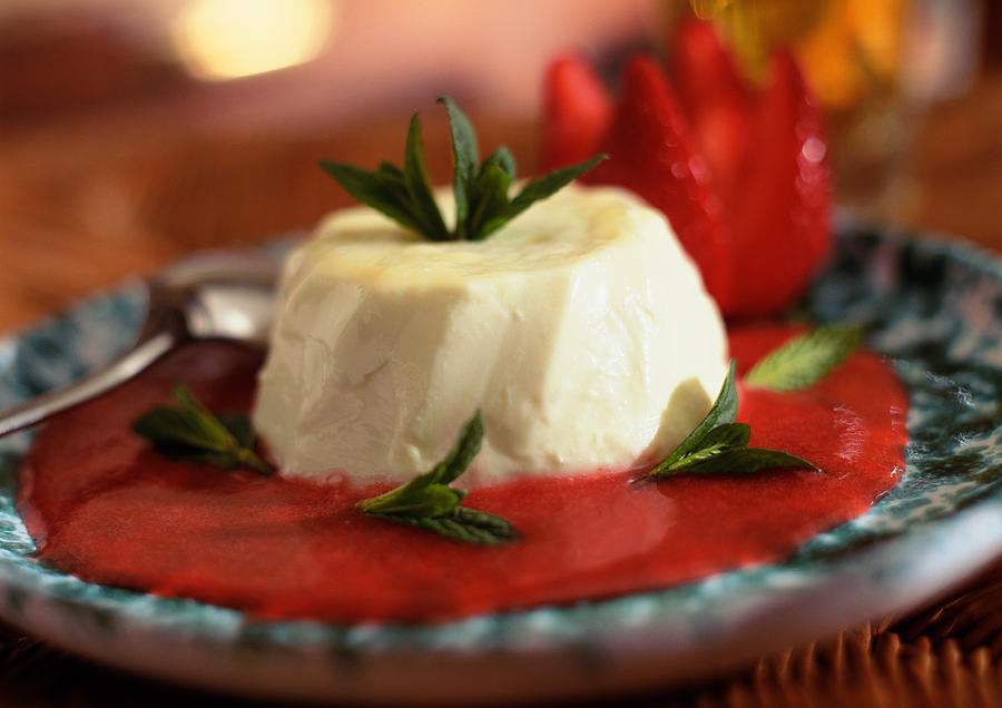Panacotta, with red fruit coulis and mint leaves, close-up Photograph by Jean-Blaise Hall