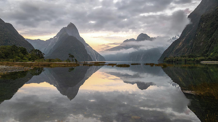 Panoramic landscape shot of sunrise in fjord with peaks shrouded in clouds and reflections on water Photograph by Peter Kolejak