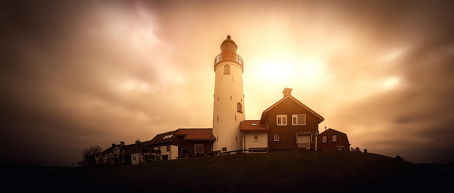 Panoramic view of a lighthouse on a hill with houses, windy sky with sun coming through the clouds. Photograph by Photo by Jeff Krol