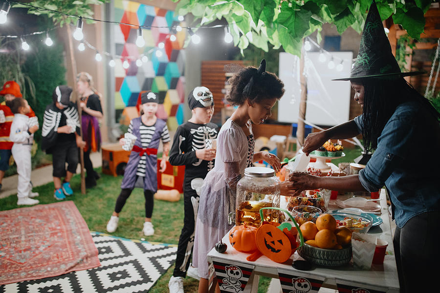 Parent serving candy and popcorn to her kids and their friends at backyard movie night Photograph by Anchiy