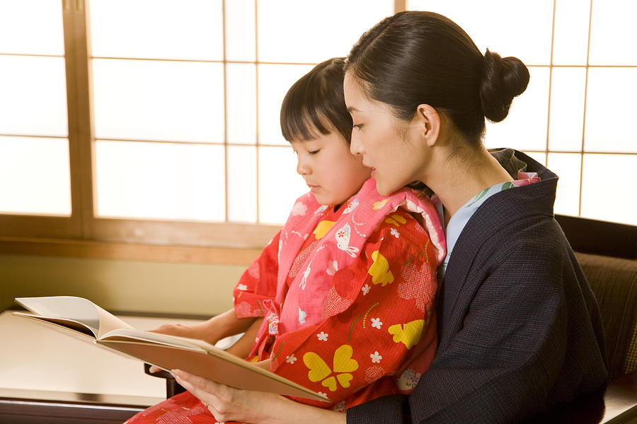 Parents and child in yukata reading book Photograph by Tagstock1