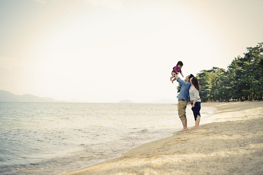 Parents lifting daughter mid air on beach Photograph by Yagi Studio