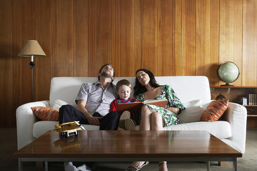 Parents relaxing on couch , in living room, while son (3-5) reads Photograph by Noel Hendrickson